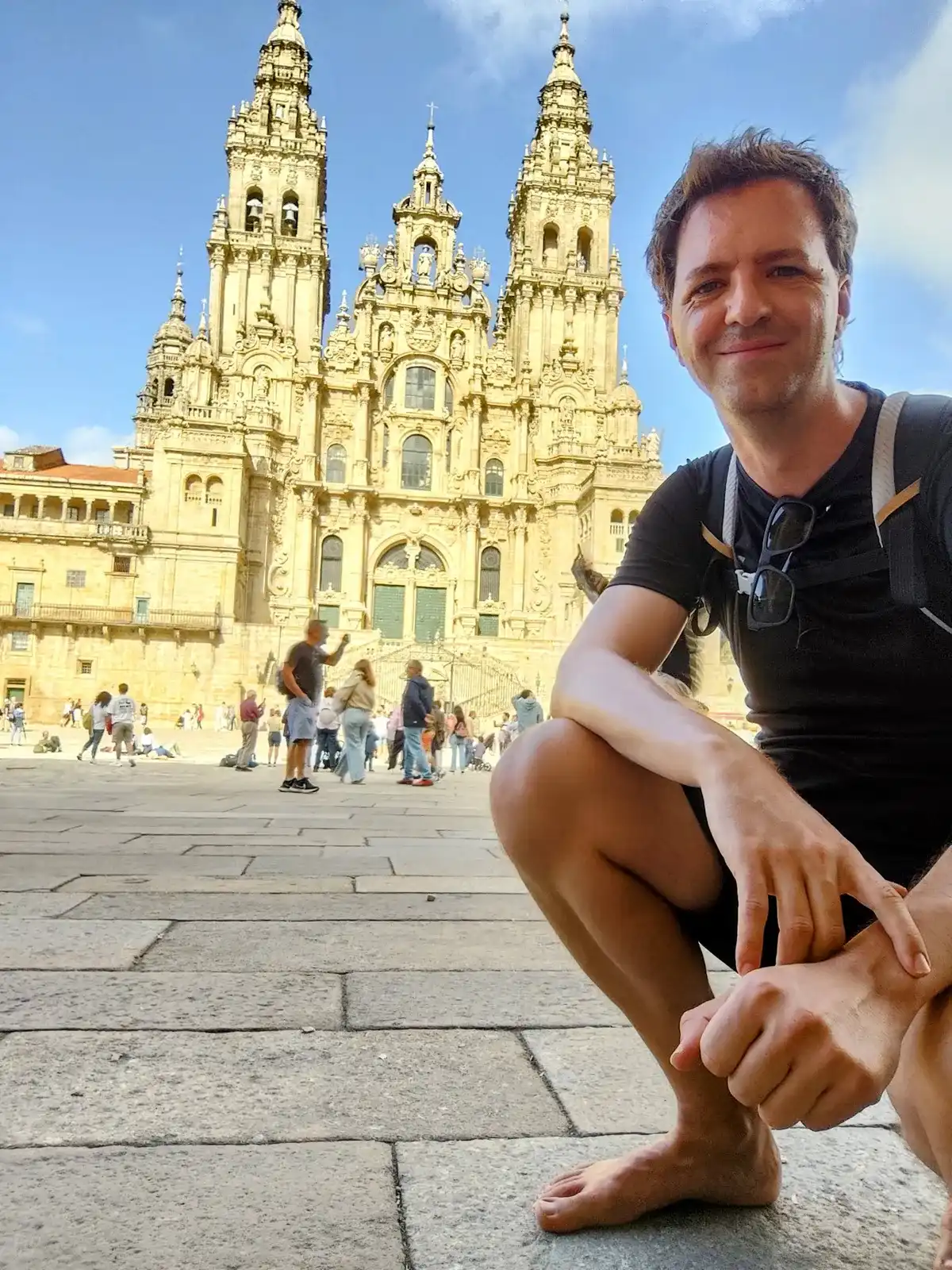 Miguel, descalzo y agachado en una plaza de piedra, con una catedral detrás