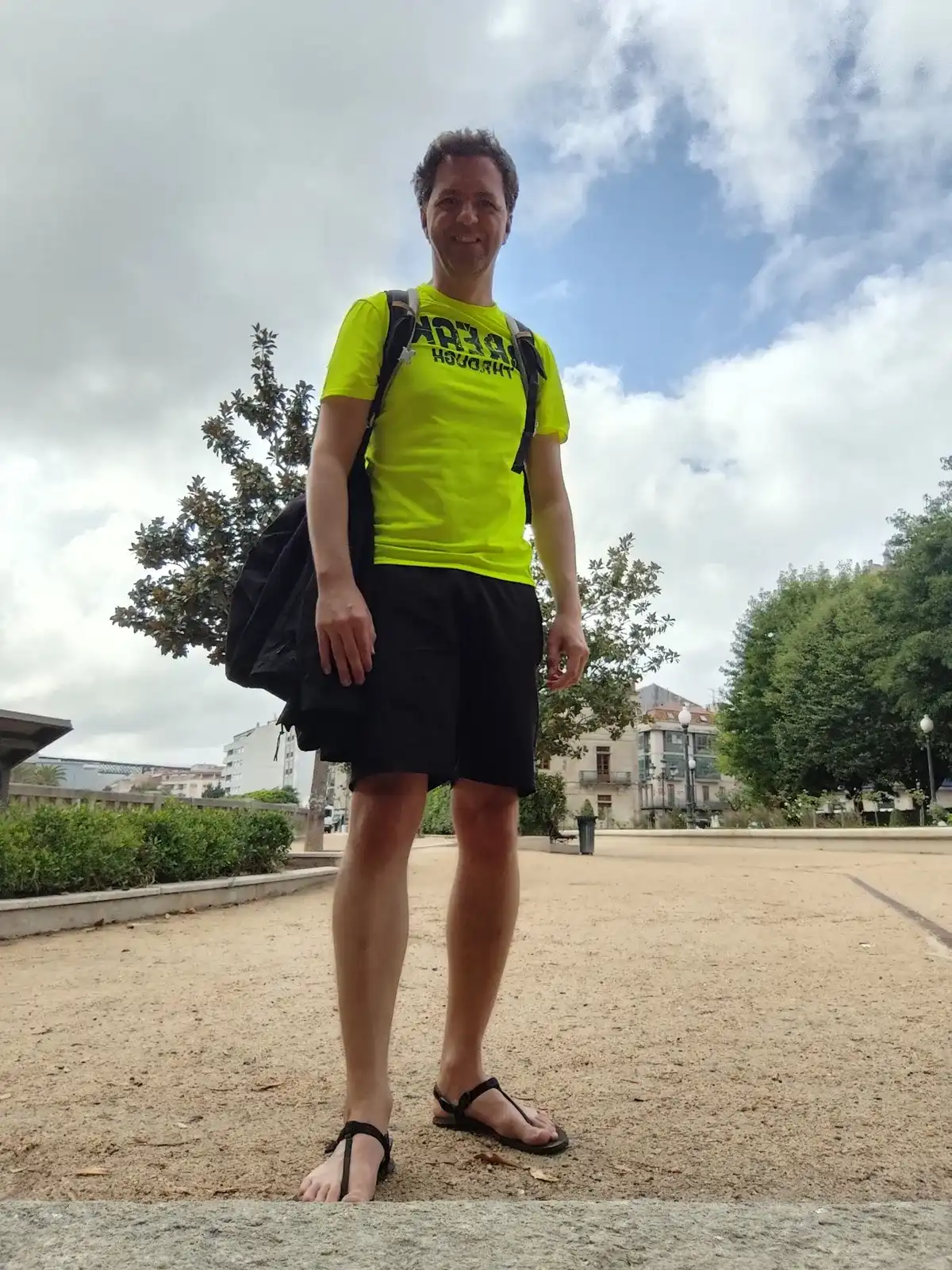 Miguel de pie en una plaza con sandalias barefoot de tiras finas y una mochila al hombro